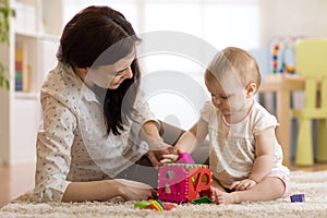 Babysitter looking after baby. Child plays with sorter toy sitting on the carpet at home photo