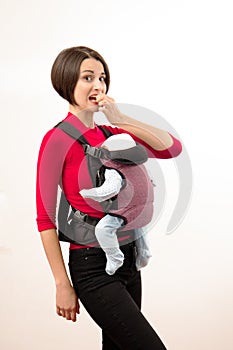 Babywearing confused young mother with baby in not ergonomic carrier. Isolated on white