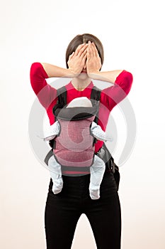 Babywearing depressed young mother with baby in wrong carrier. Isolated on white