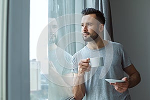 Bachelor man daily routine standing near the window single lifestyle concept drinking coffee thinking