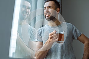 Bachelor man daily routine standing near the window single lifestyle concept drinking tea dreaming