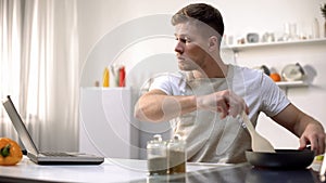 Bachelor preparing meal in pan, reading recipe and cooking tips online, courses