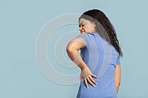 Back ache. Unrecognizable black lady touching back, suffering from pain in lower back and spasms, blue background