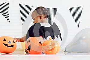 Back of adorable African baby kid dressing up in vampire fancy Halloween costume with black bat wings, cheerful little cute child