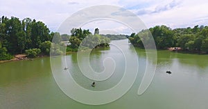 Back aerial flight over fisherman sitting in boat further pictorial landscape with forest and river with fishing boats