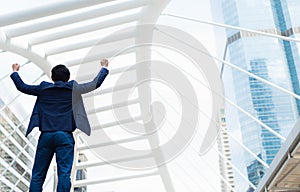 Back of Asian businessman stand and raising up his two hands to cheerful and celebrated his successful in career and mission.