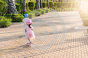 Back Asian little kid boy and girl wear safe helmet play kick board on road in park outdoors on summer day