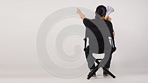 Back of Asian man sitting on black director chair. He pointing and holding a megaphone on white background. full backal
