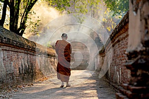 Back of Asian monk walk on the way along with old wall of ancient palace or building with linne beam light