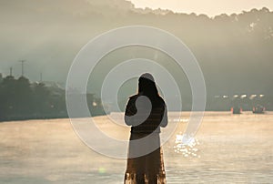 Back of Asian woman tourist standing alone look at view at lakeside of Ban Rak Thai Village with fog rising on the lake in the