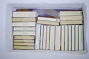 Back of assortment of books in a white shelf with view to the next room in a white textured wall, closeup