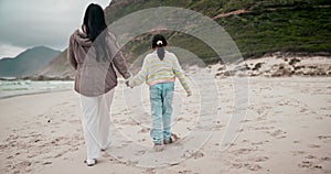 Back, beach and a mother holding hands with her daughter while walking outdoor on sand by the coast. Family, children