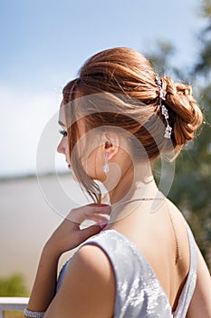 Back of beautiful girl in tender prom dress on river bank background. Female portrait on spring landscape.