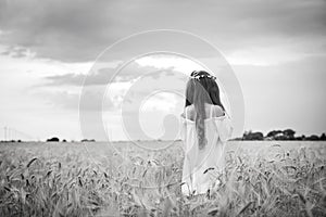 Back of a beautiful girl in a wheat field with long hair and a wreath.