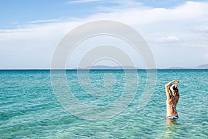 Back of beautiful woman wearing blue bikini standing in the water on Mediterranean sea coast, Cesme, Ilica beach, Turkey