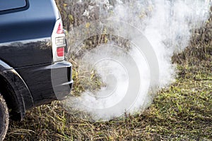 The back of the black car with the emission of smoke from the exhaust pipe on the background of nature photo