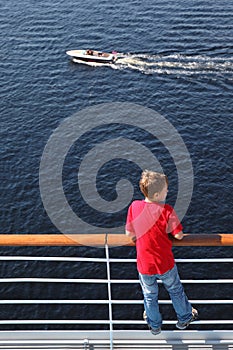 Back of boy standing at railing on deck of ship