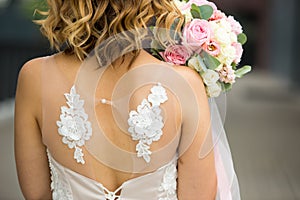 Back of the bride in a white wedding dress close-up. Bride`s bouquet of roses in pastel colors, curls. Angel wings in the decorati
