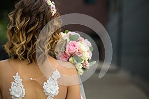 Back of the bride in a white wedding dress close-up. Bride`s bouquet of roses in pastel colors, curls. Angel wings in the decorati