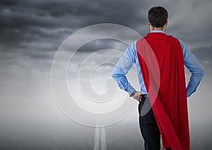 Back of business man superhero with hands on hips against road and stormy sky