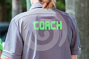 Back of a coach`s grey shirt with the green word Coach written o