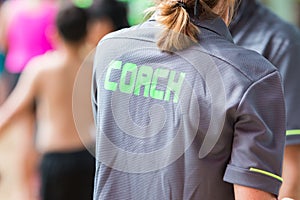 Back of a coach`s grey shirt with the green word Coach written o