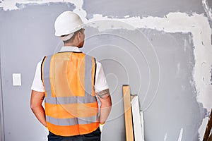 The back of a construction worker in uniform as he faces work in progress