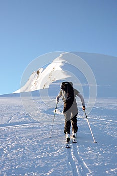 A back country skier heads to a high alpine summit on skis in winter