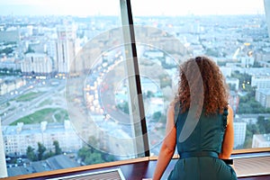 Back of curly woman in dress looking through bid