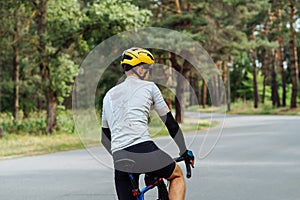 The back of a cyclist`s man trains outside the city on an asphalt road in the woods, view from the back