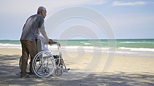 Back elderly woman disabled sitting in wheelchair and husband is a wheelchair user on the beach