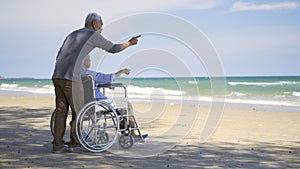 Back elderly woman disabled sitting in wheelchair and husband is a wheelchair user on the beach