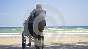 Back elderly woman disabled sitting in wheelchair and husband is a wheelchair user on the beach