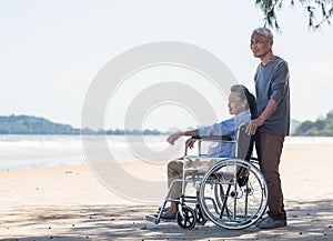 back elderly woman disabled sitting in wheelchair and husband is a wheelchair user on the beach