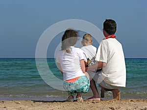 Back family of three sit on beach