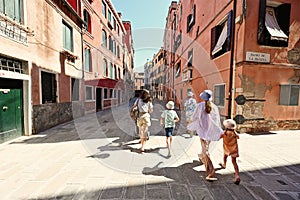 Back of family tourists walk in Ramo De La Piscina street, Venice, Italy