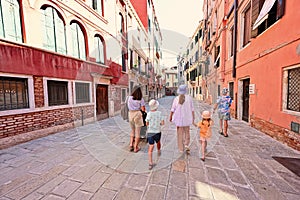 Back of family tourists walk in Ramo De La Piscina street, Venice, Italy