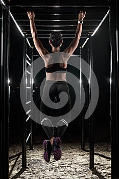 Back of female athlete with fit body hanging on the pullup bar