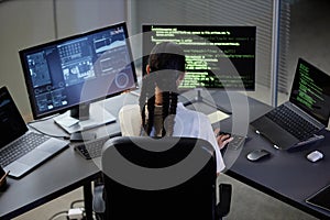 Back of Female IT Programmer Coding on Multiple Computers at Desk in Office