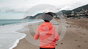 Back follow shot of young woman is running on beach in the morning. Sporty motivated female is jogging on seashore. Female tourist