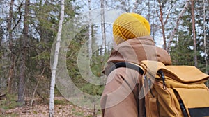 Back frame of a young traveller with yellow backpack walking in the forest.