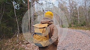 Back frame of a young traveller with yellow backpack walking in the forest.