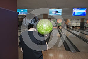 The back of a girl who plays holds a ball for bowling before the throw. The bowling game.
