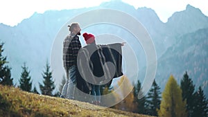 Back of happy hipster family. Girl shows guy mountains and meadows. Silhouette of couple in front of hills view. Two