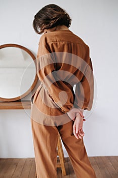 Back image of sexy woman in a brown jumpsuit holding hands behind her back