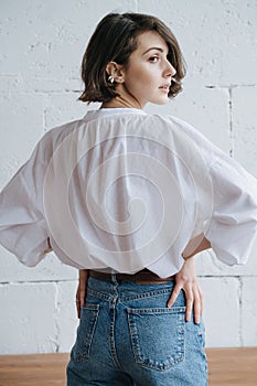 Back image of a young woman looking to side. She wears shirt and jeans