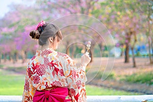 Back of Japanese woman in traditional kimono dress enjoy travel and holding dango at bridge in spring festival
