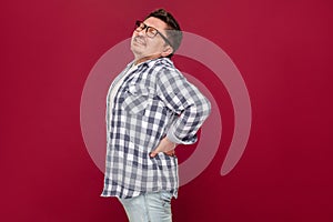 Back, kidney or spine pain. Portrait of sad middle aged man in casual checkered shirt and eyeglasses standing and holding his