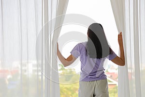 Back of lady who is opening curtain in the bedroom to see city view in the morning with copy space