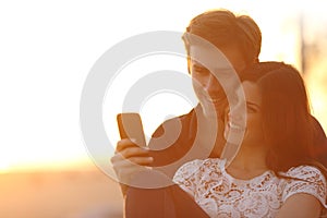 Back light of a couple sharing a smart phone